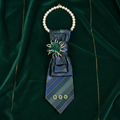 Iridescent teal navy stripe necktie necklace with emerald green marquise crystal starburst brooch displayed as flat lay on forest green velvet