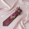 Dusty rose mauve necktie necklace with gathered rose accent and fuchsia crystal brooch displayed as flat lay on blush pink silk surface