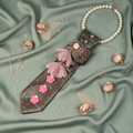 Sage green gold floral tapestry necktie necklace with pink rhinestone accents and feather flower displayed as flat lay on sage silk