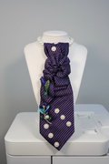 Purple striped necktie necklace with pearl accents and jeweled floral brooch on a soft gray background