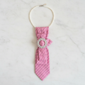 Soft pink striped necktie necklace with pearl and rhinestone brooch displayed as flat lay on white marble surface
